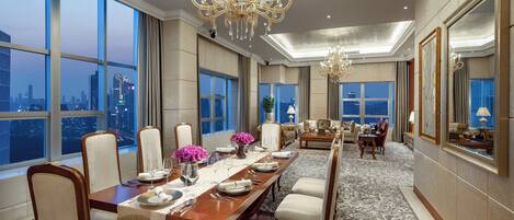 Un comedor amplio con una larga mesa dispuesta para una comida, ventanas grandes que ofrecen vistas de la ciudad y elegantes candelabros.
