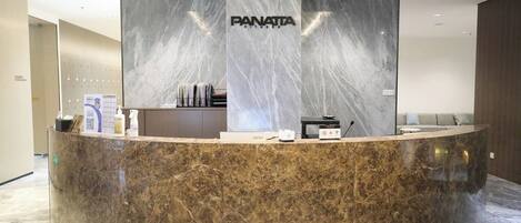 A reception desk with a marble top, a large 'PANATTA' sign, and a counter with various amenities.