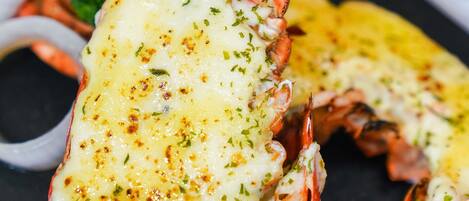 A lobster tail with melted cheese and herbs, served with vegetables and a dipping sauce.