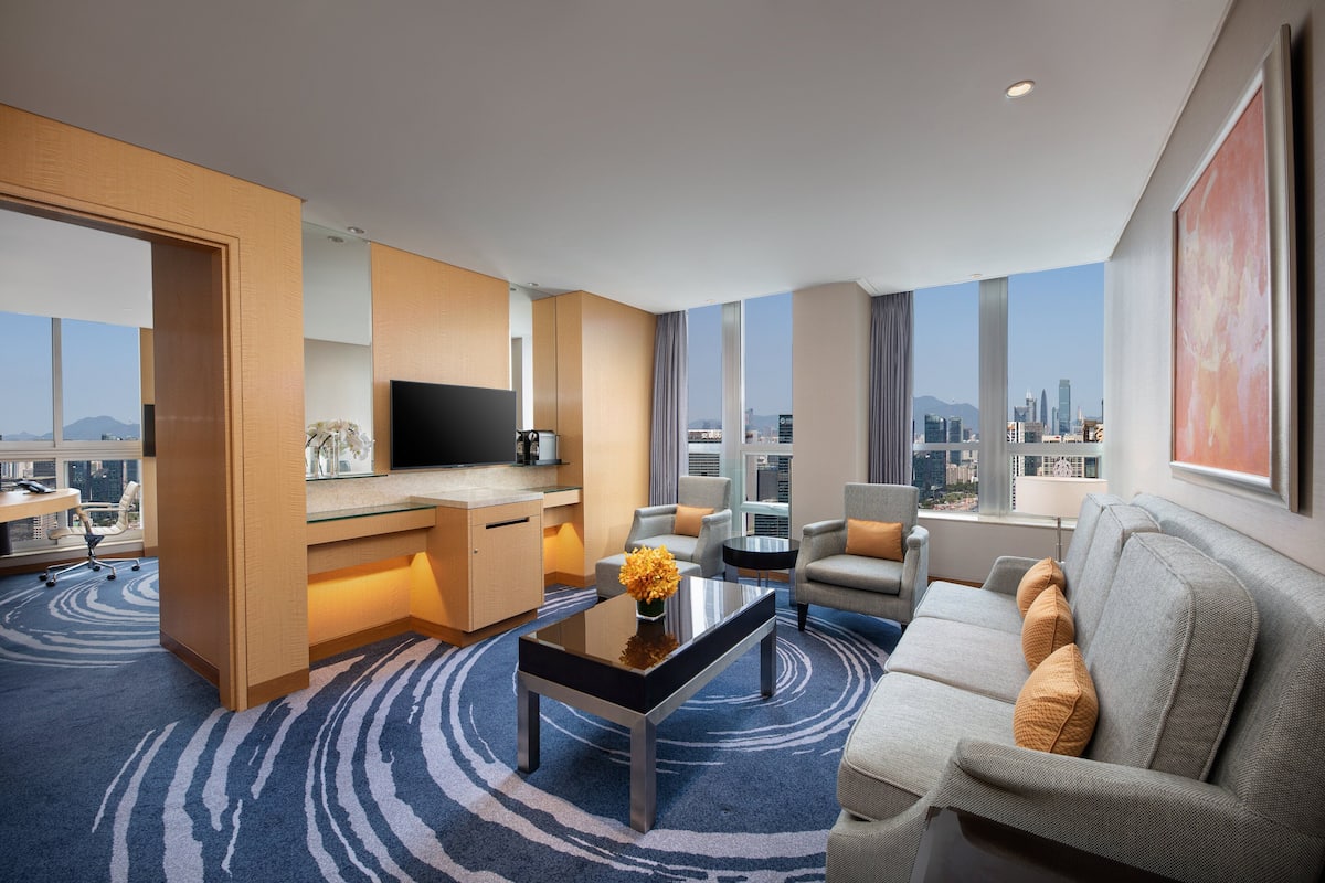 Ein modernes Hotelzimmer mit Blick auf die Stadt, einem Flachbildfernseher, einer Essecke und einem Sofa mit dekorativen Kissen.