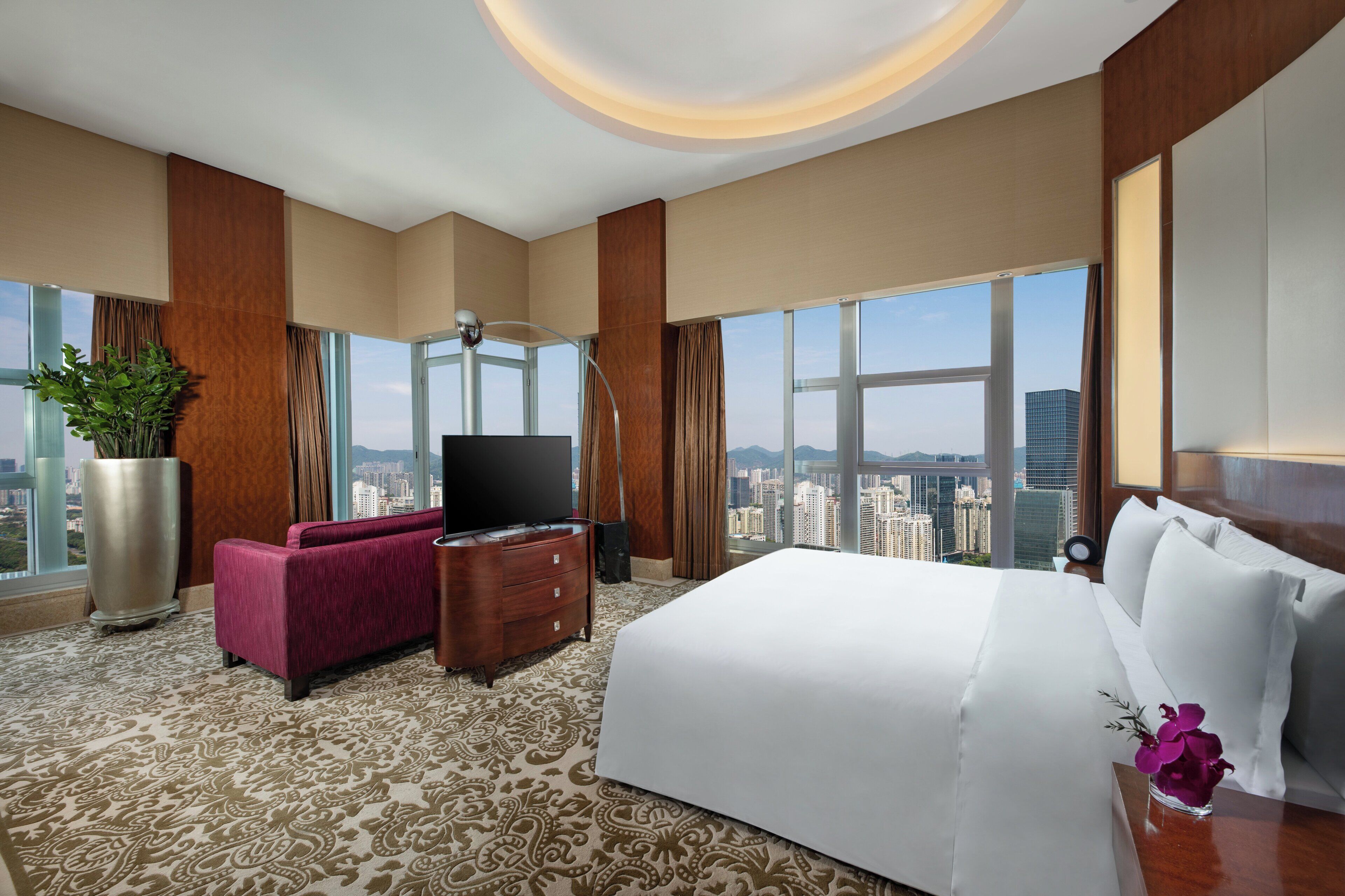 Ein Hotelzimmer mit einem großen Bett, einem Fernseher, einer Couch und Blick auf die Stadt.