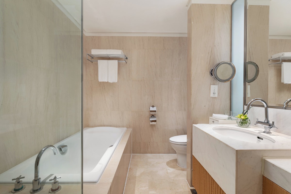 Un baño moderno con cabina de ducha de vidrio, bañera, inodoro y lavamanos con espejo.