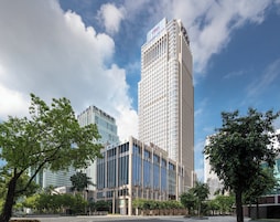Un edificio moderno de gran altura con una entrada destacada y arbolado circundante.