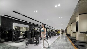 A modern gym with various exercise equipment, a mirrored wall, and a row of treadmills.