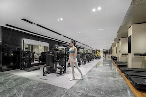 Un gimnasio moderno con diversos equipos de ejercicio, un espejo grande y una fila de cintas de correr.