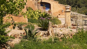 A rustic building with a stone facade, a large arched doorway, and a garden with various plants and a cactus. - Agroturisme Es Picot (Manacor)