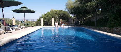 Una piscina al aire libre, sombrillas, sillones reclinables de piscina