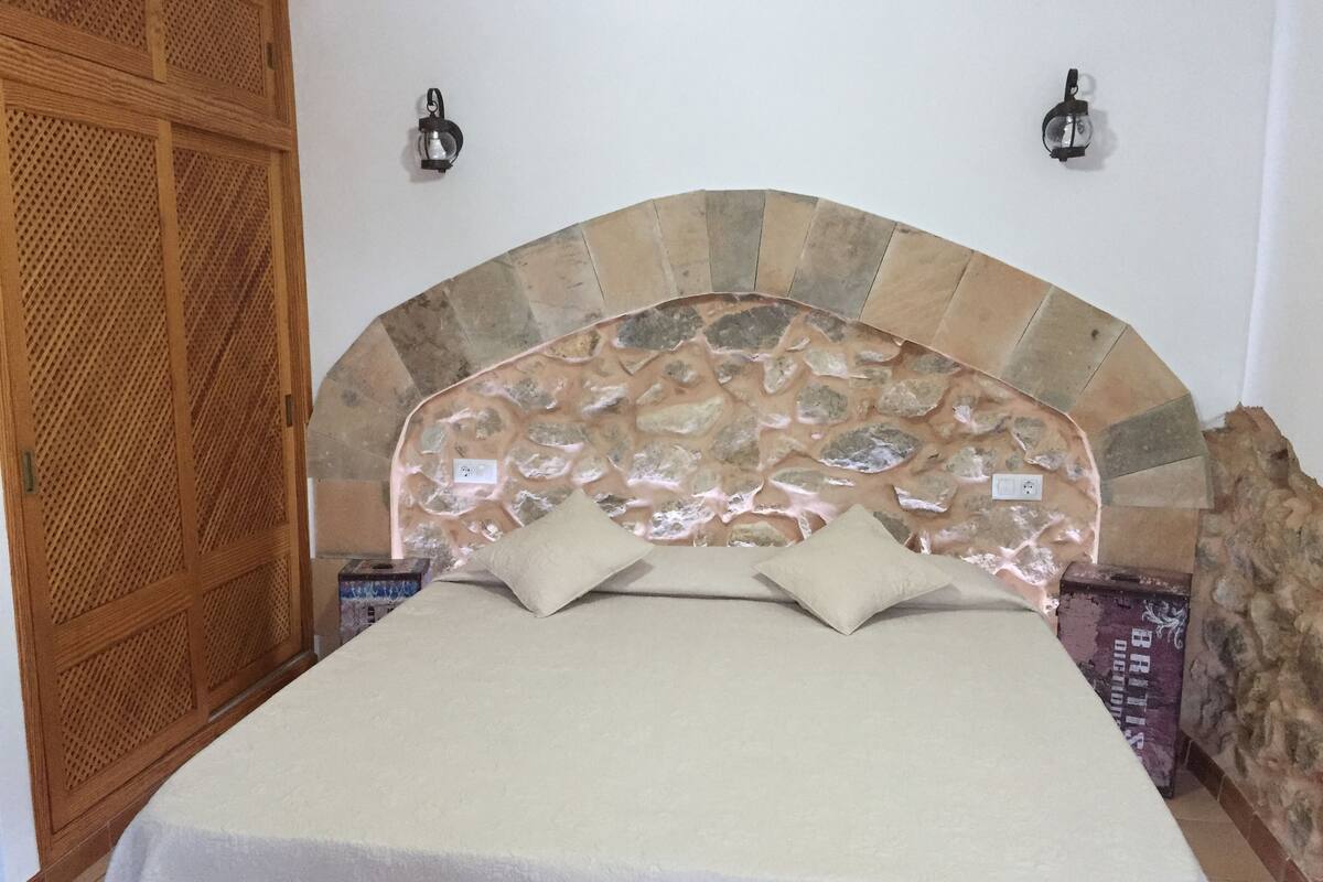 A bed with a stone headboard, two wall-mounted lights, and a wooden door.