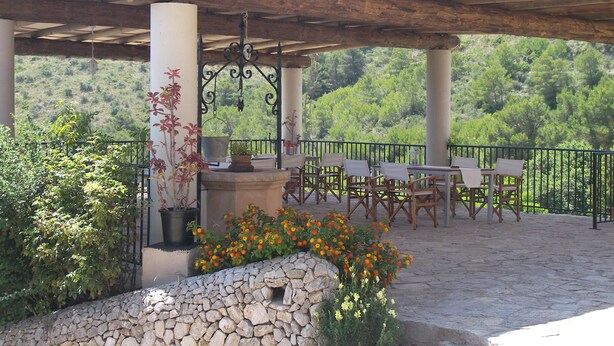 A covered outdoor seating area with stone walls, a pergola, and a view of a green hillside. - Agroturisme Es Picot (Manacor)