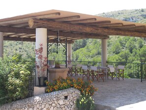 A covered outdoor seating area with stone walls, a pergola, and a view of a green hillside. - Agroturisme Es Picot (Manacor)