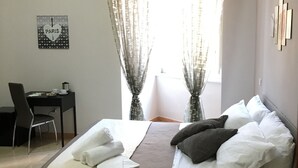 A hotel room with a bed, a desk, a chair, a lamp, and a window with curtains. - Soggiorno Paradiso due (Naples)