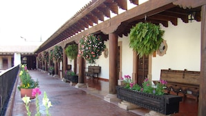 Un pasillo cubierto con suelo de baldosas, columnas de madera y macetas colgantes con flores.