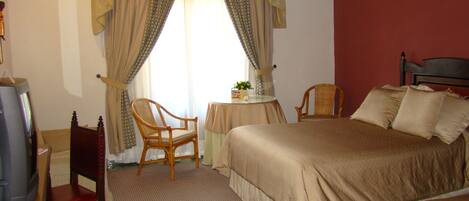 A hotel room with a bed, two chairs, a small table, and a television.