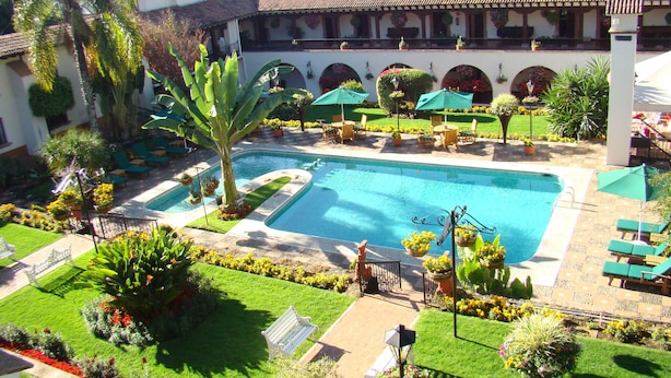 Zona de piscina con una pileta rectangular, rodeada de césped, plantas en macetas y mobiliario de exterior.