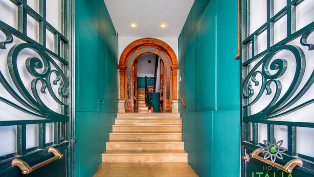 A hotel entrance with teal walls, a wooden staircase, and metal gates. - Hotel Italia (Lisbon)