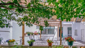 A covered outdoor seating area with potted plants and a view of a building with white walls and a window. - Hotel Italia (Lisbon)