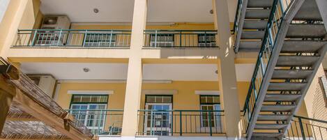 Un hotel de varios pisos con balcones, un patio con mobiliario exterior y un cielo despejado.