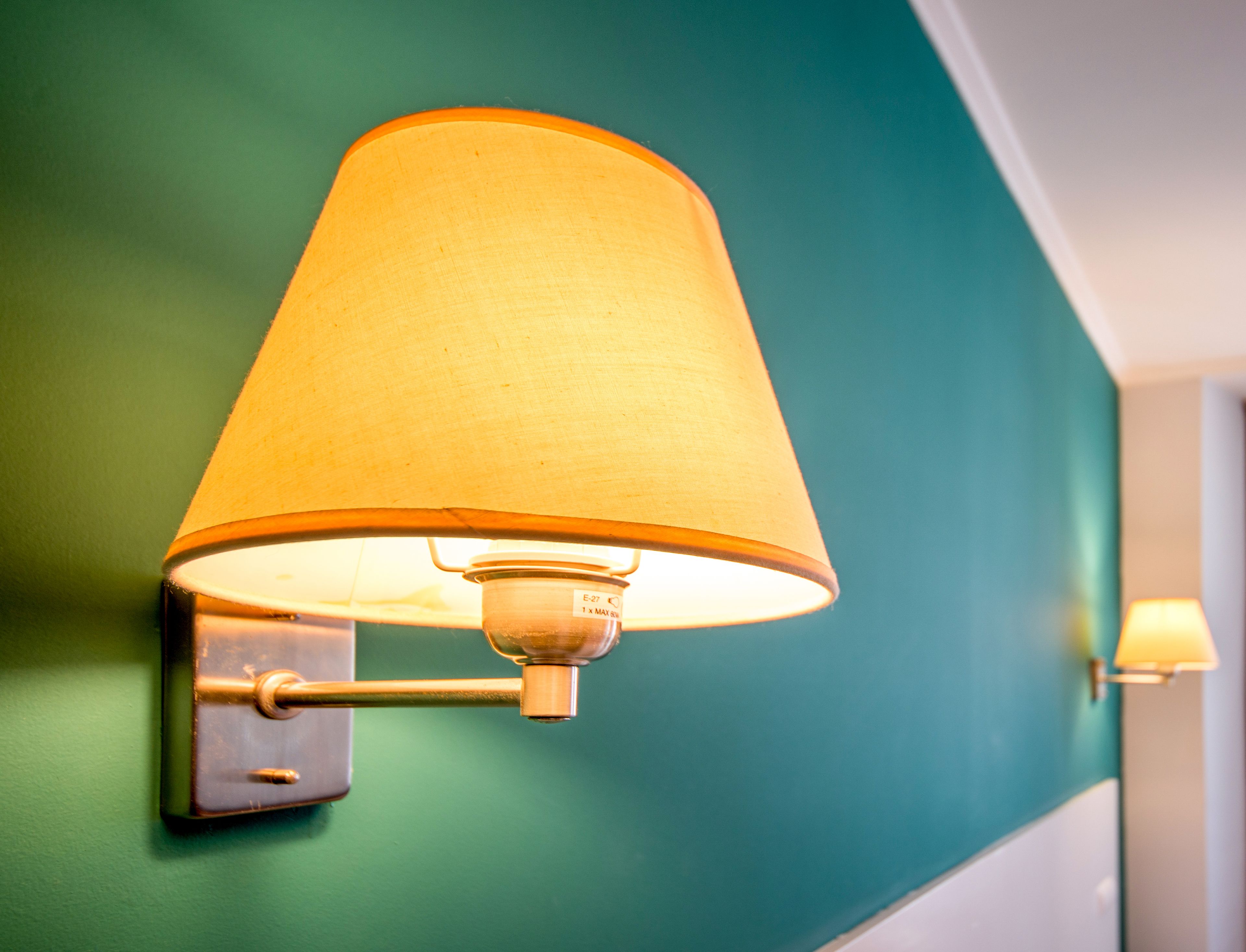 Una lámpara de pared con pantalla de tela sobre una pared color turquesa.