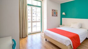 A bedroom with a large bed, a window with curtains, a teal accent wall, and a ceiling light. - Hotel Italia (Lisbon)
