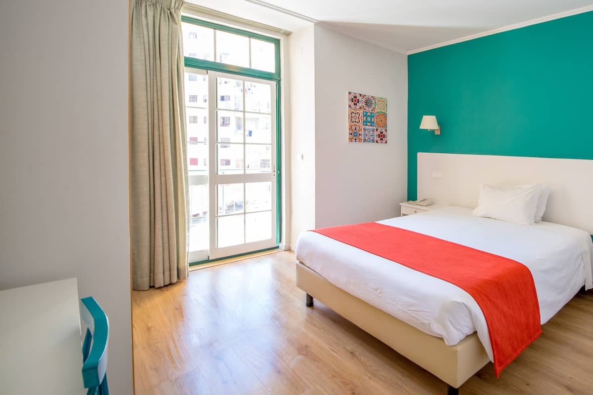 A bedroom with a large bed, a window with curtains, a teal accent wall, and a ceiling light.