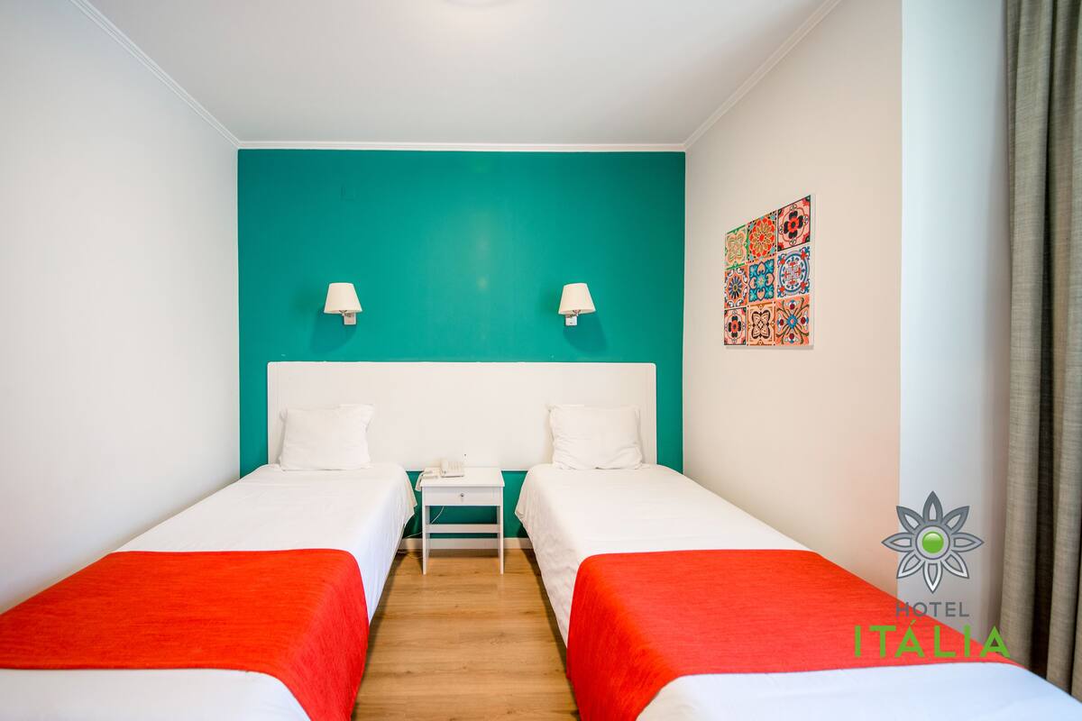 A hotel room with two beds, a teal accent wall, a small table, and a decorative tile wall art piece.