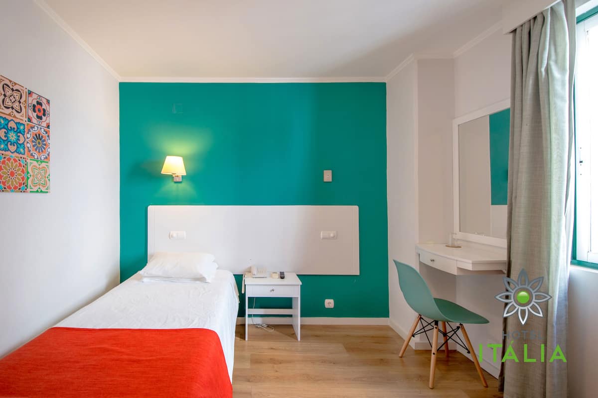 A hotel room with a bed, desk, chair, and a teal accent wall.