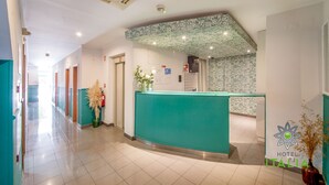 A hotel reception area with a teal reception desk, a floral-patterned wall, and a tiled floor. - Hotel Italia (Lisbon)