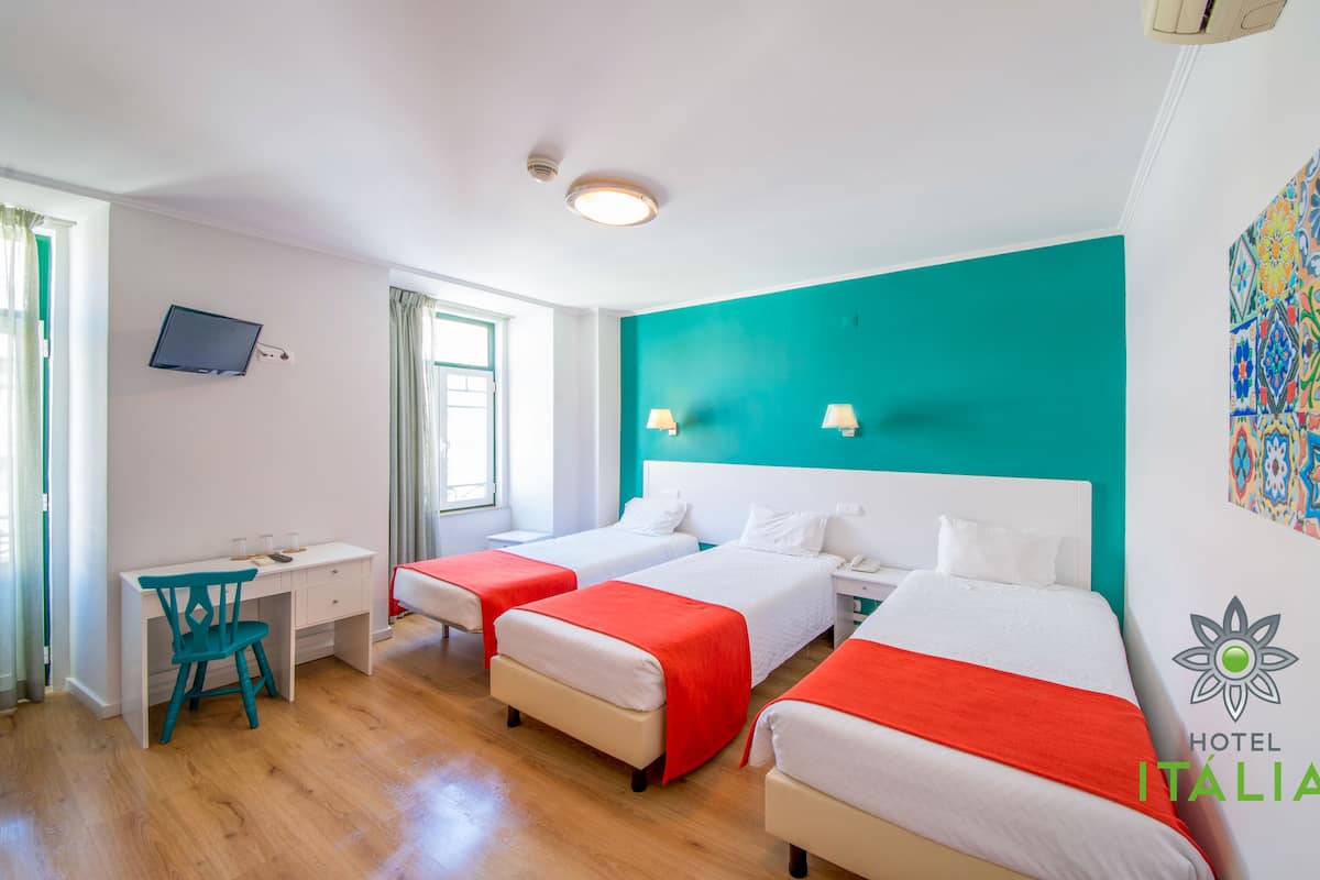 A hotel room with two beds, a desk, a chair, a TV, and a window with curtains.