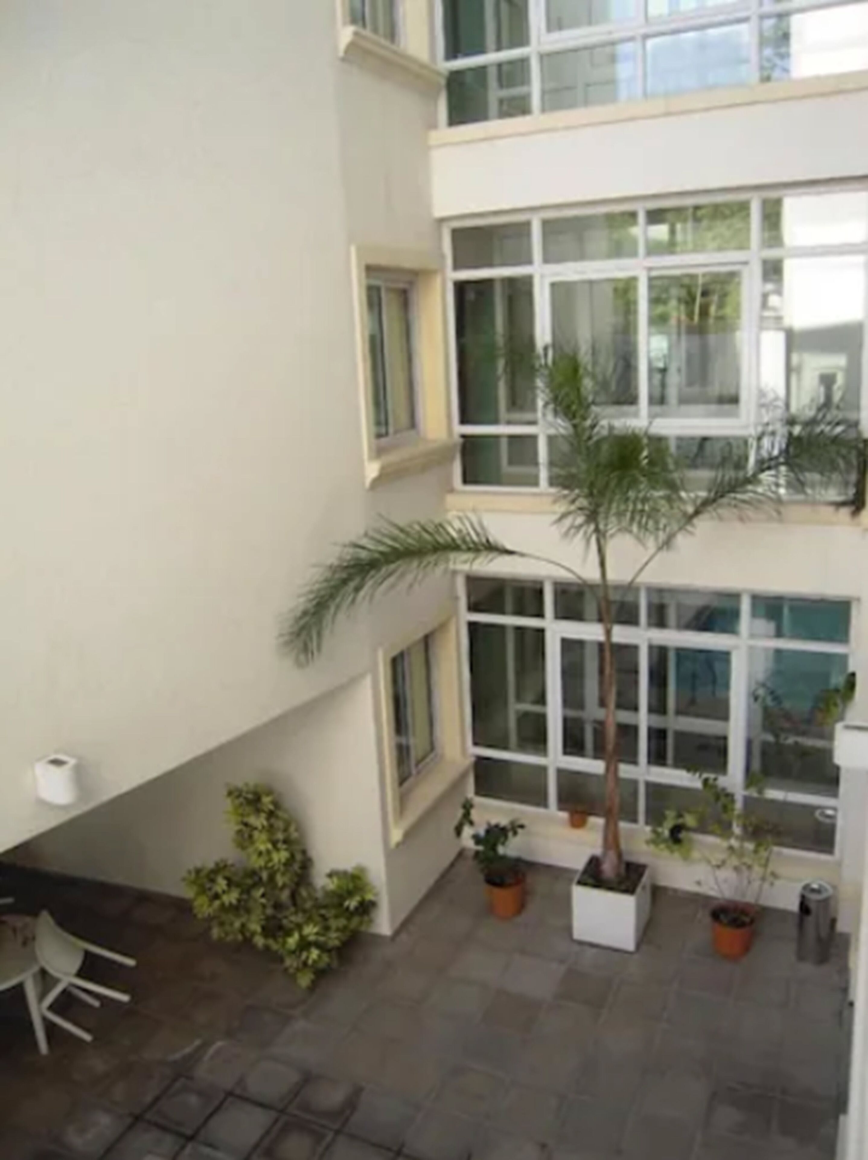 A multi-story building with large windows, a tiled patio area with potted plants, and a white chair.