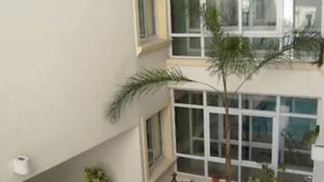 A multi-story building with large windows, a tiled patio area with potted plants, and a white chair.