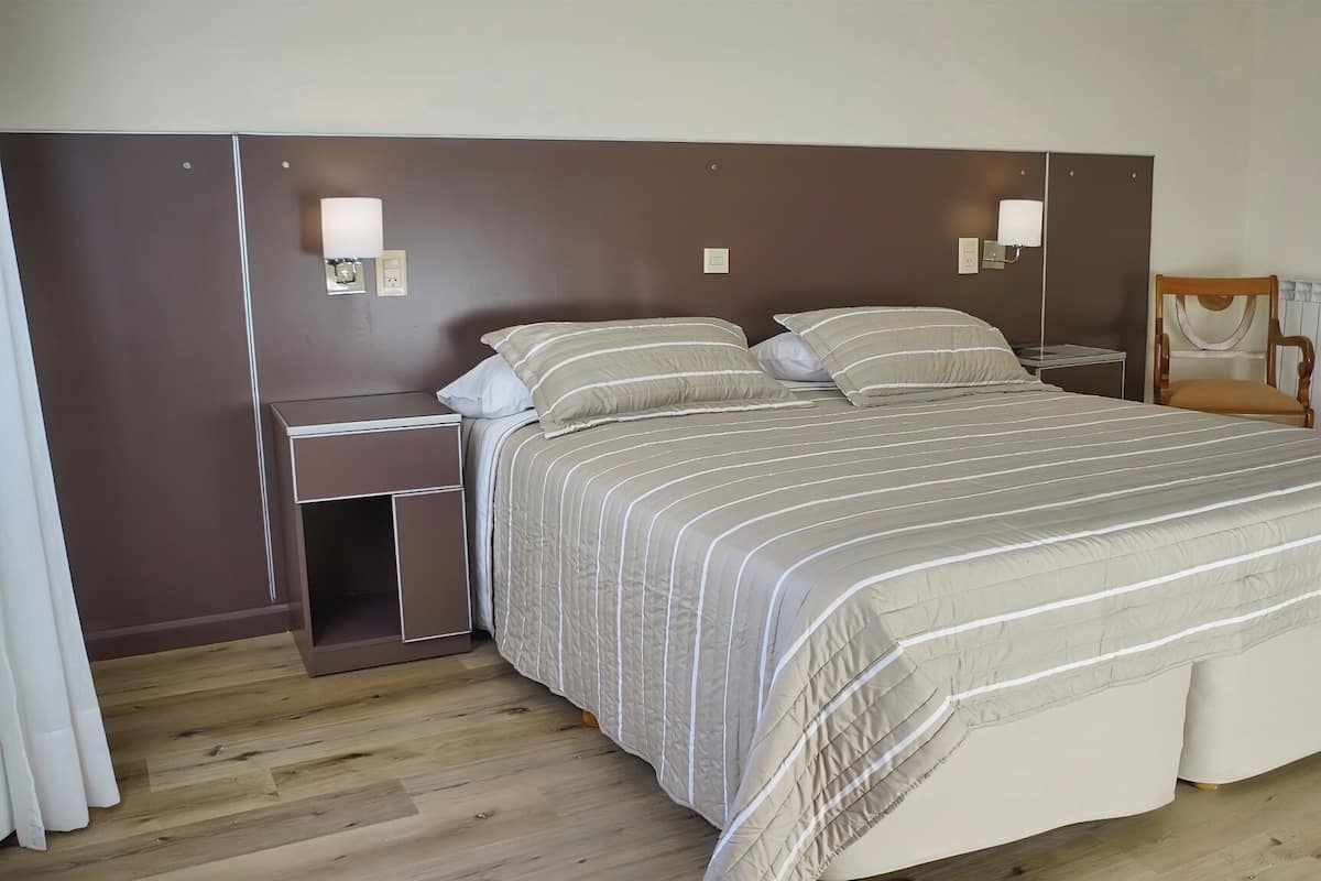 A neatly arranged bedroom with a large bed, a bedside table, a chair, and a nightstand.