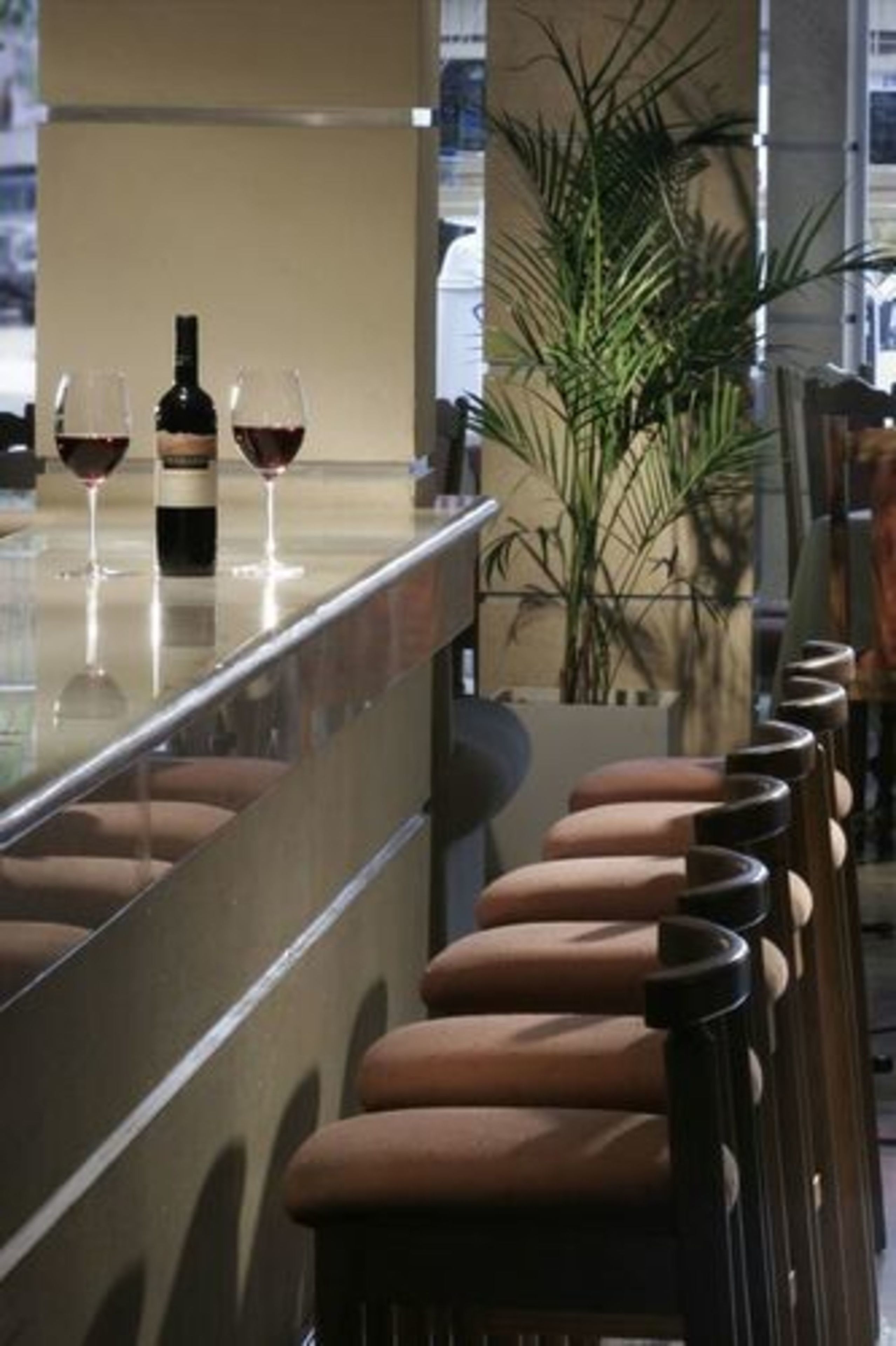 Un coin bar avec une bouteille de vin et deux verres posés sur le comptoir, entouré de tabourets de bar marron à coussin.