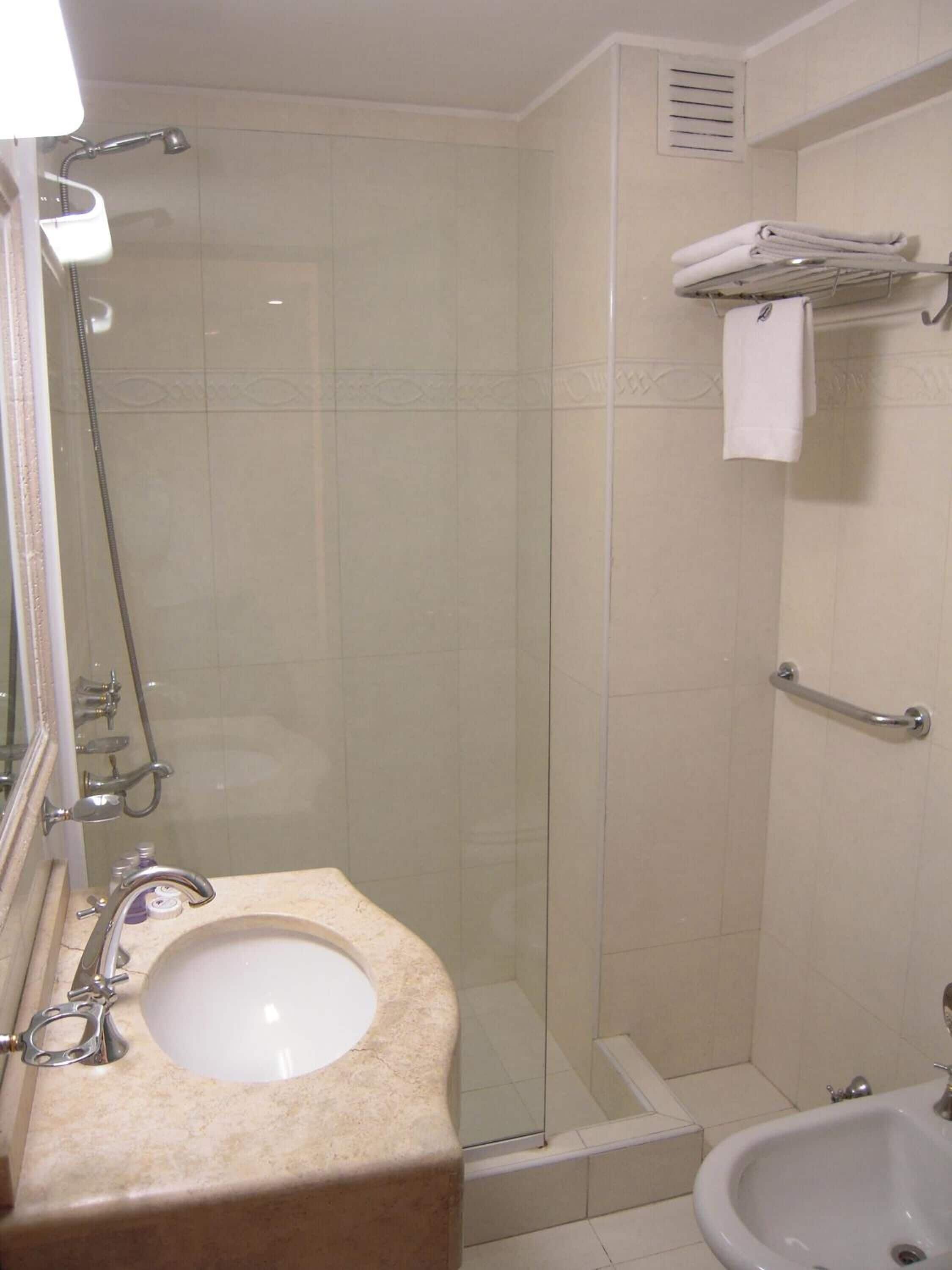 Un baño con ducha de vidrio, lavamanos con espejo y un bidé.
