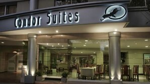 Exterior de Condor Suites con un letrero iluminado, amplios ventanales y un área de comedor visible en el interior.