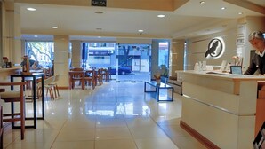 Un hall de hotel con mostrador de recepción, zona de estar y vistas a la calle a través de amplios ventanales.