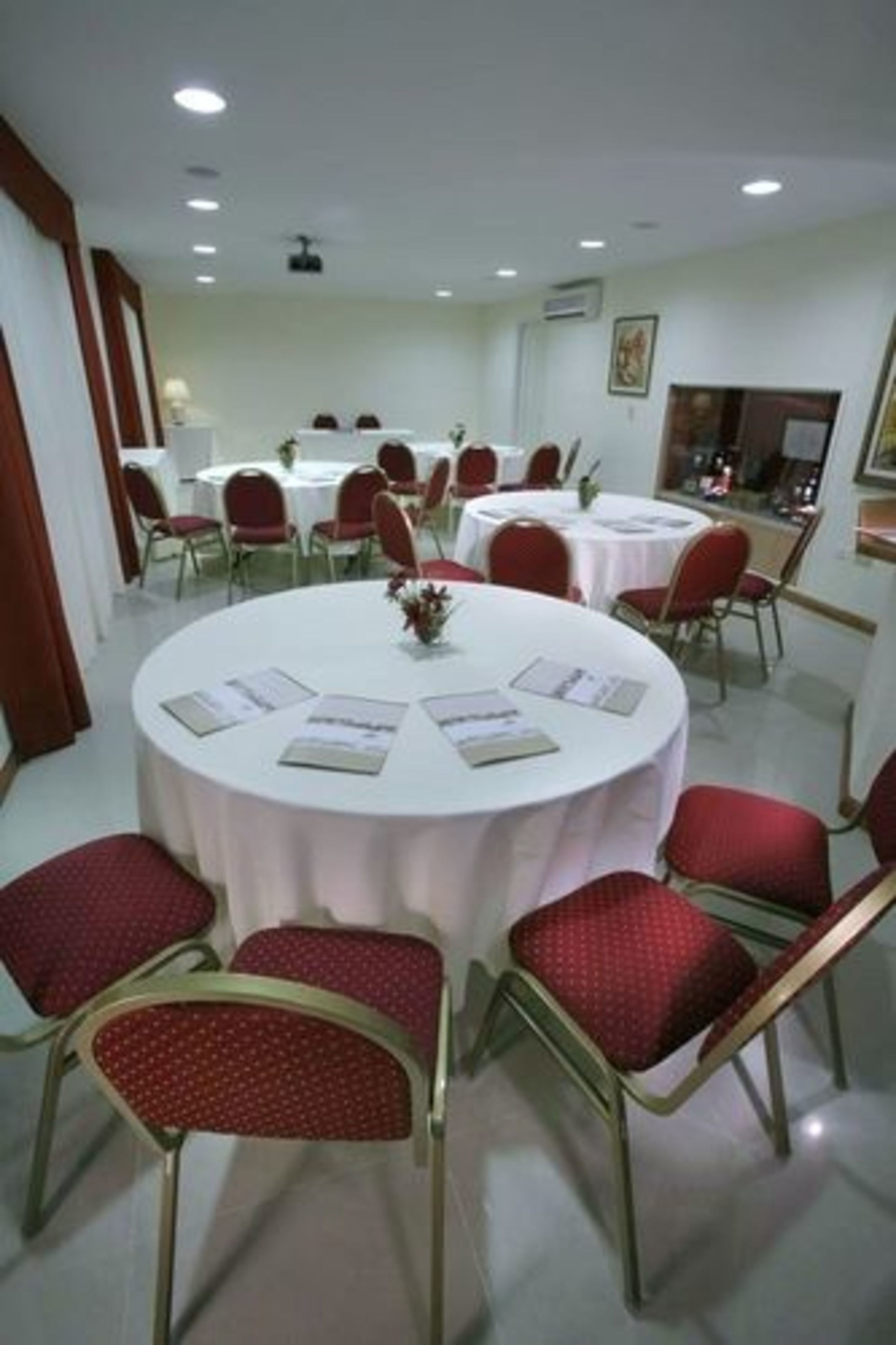 A conference room with round tables, red chairs, and white tablecloths.