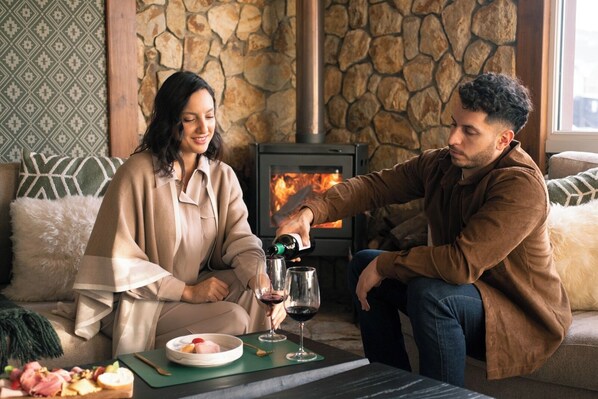 A cozy room with a stone wall, a fireplace, and a dining table with food and wine. -  Lennox Hotel Ushuaia (Ushuaia)
