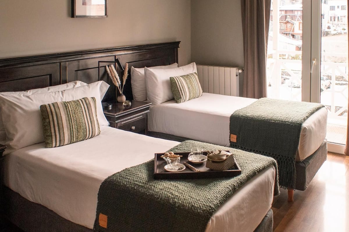 A hotel room with two beds, a view of the outside, and a small table with a tray of food.