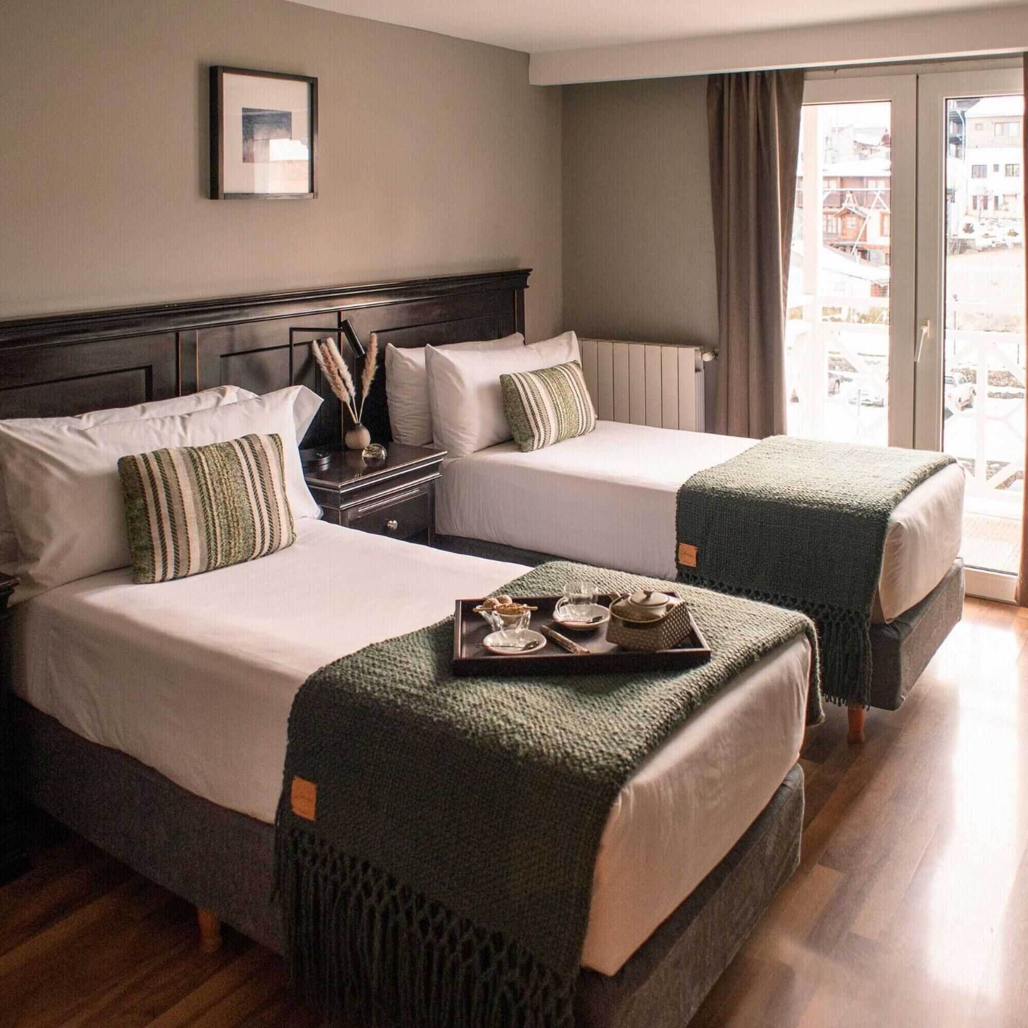 A hotel room with two beds, a nightstand, a framed picture on the wall, and a view of the outside through a large window.
