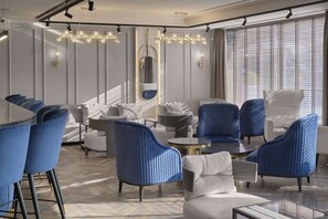 Un área de descanso moderna con asientos tapizados en azul y blanco, una mesa redonda y un espejo grande en la pared.