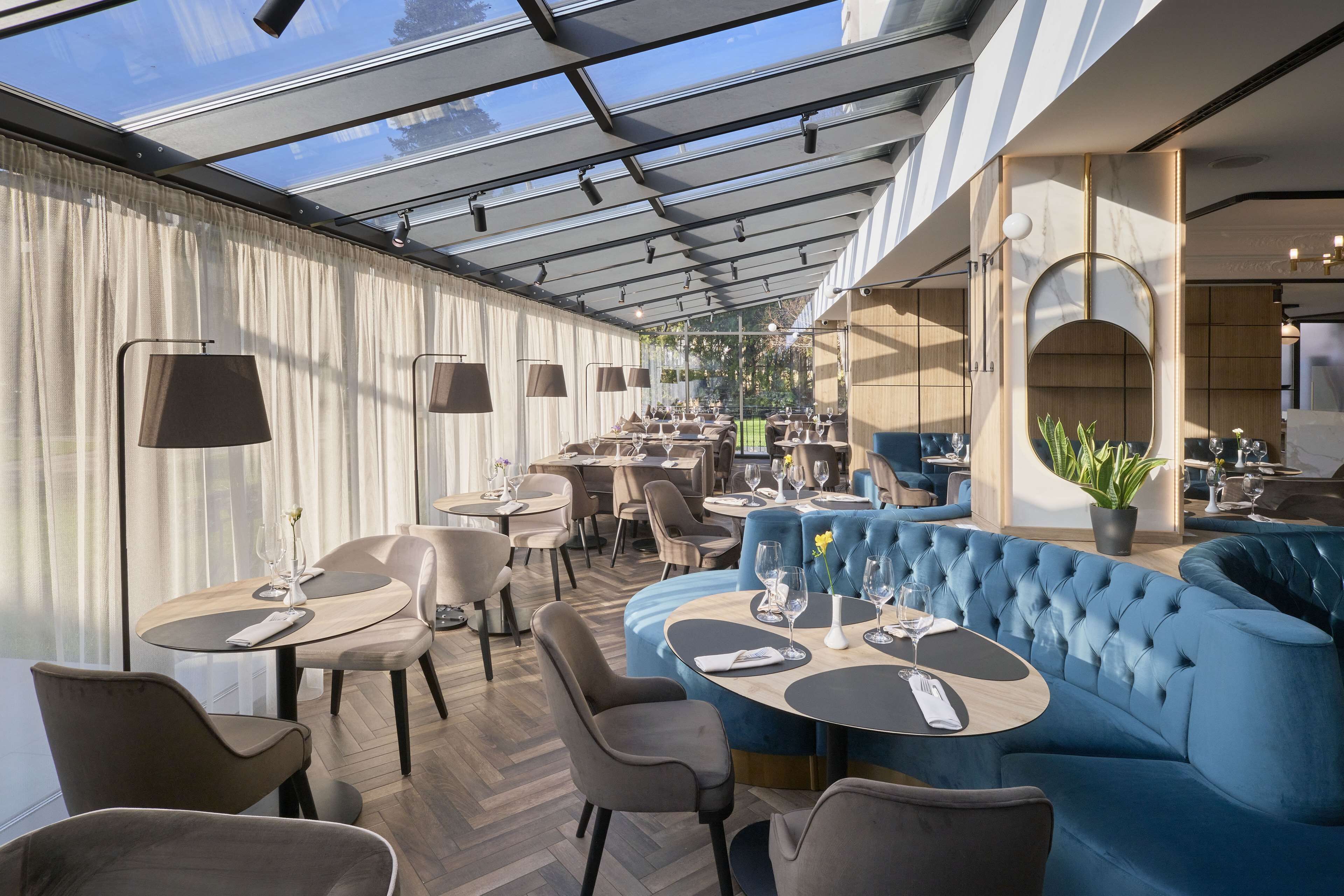 Un restaurante moderno con techo de vidrio, asientos tapizados en azul y diversas mesas de comedor.