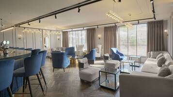 A modern hotel room with a dining area, seating, and a large window with curtains.