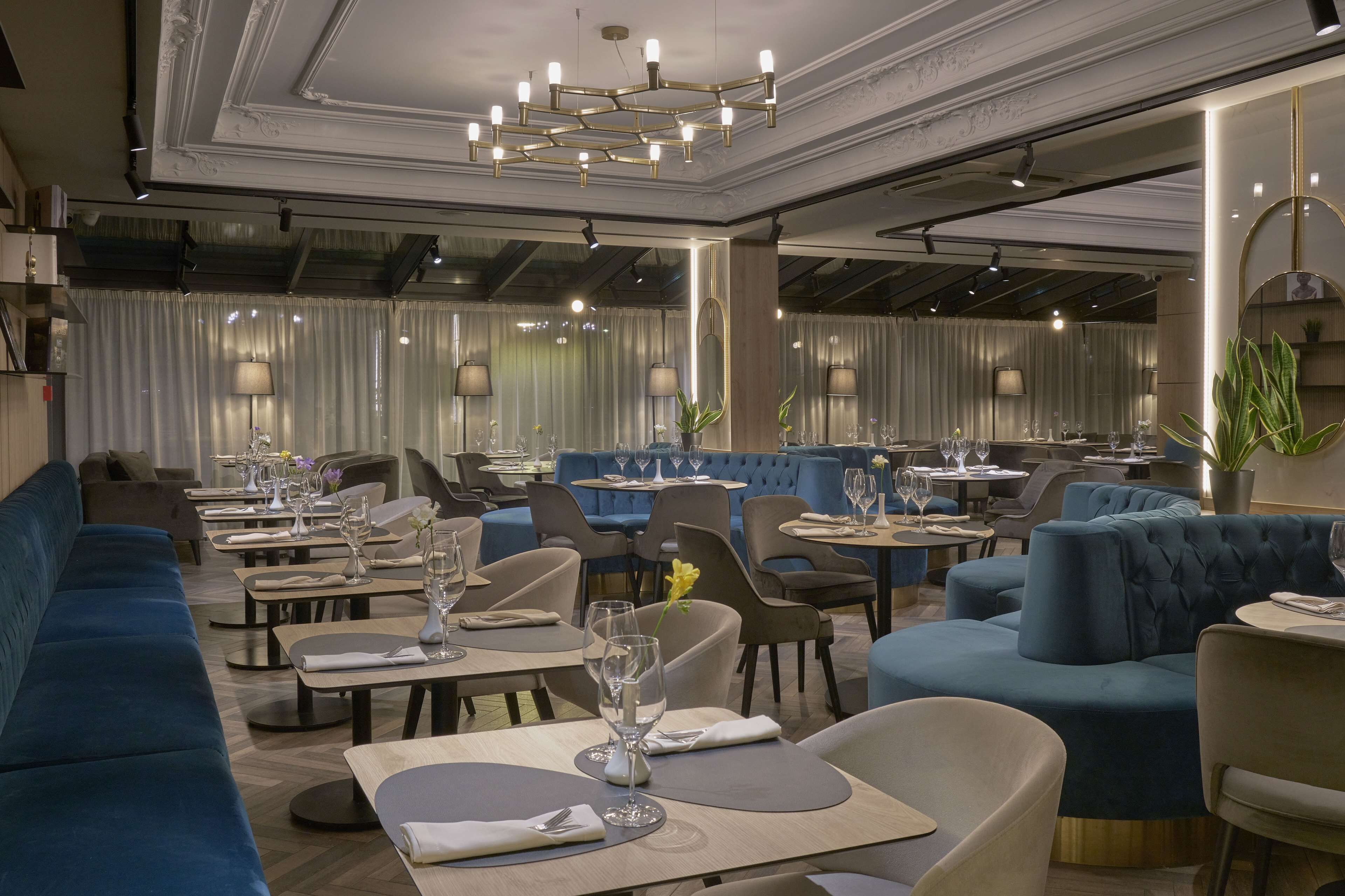 Un restaurante moderno con asientos tapizados en azul, mesas redondas e iluminación ambiental.