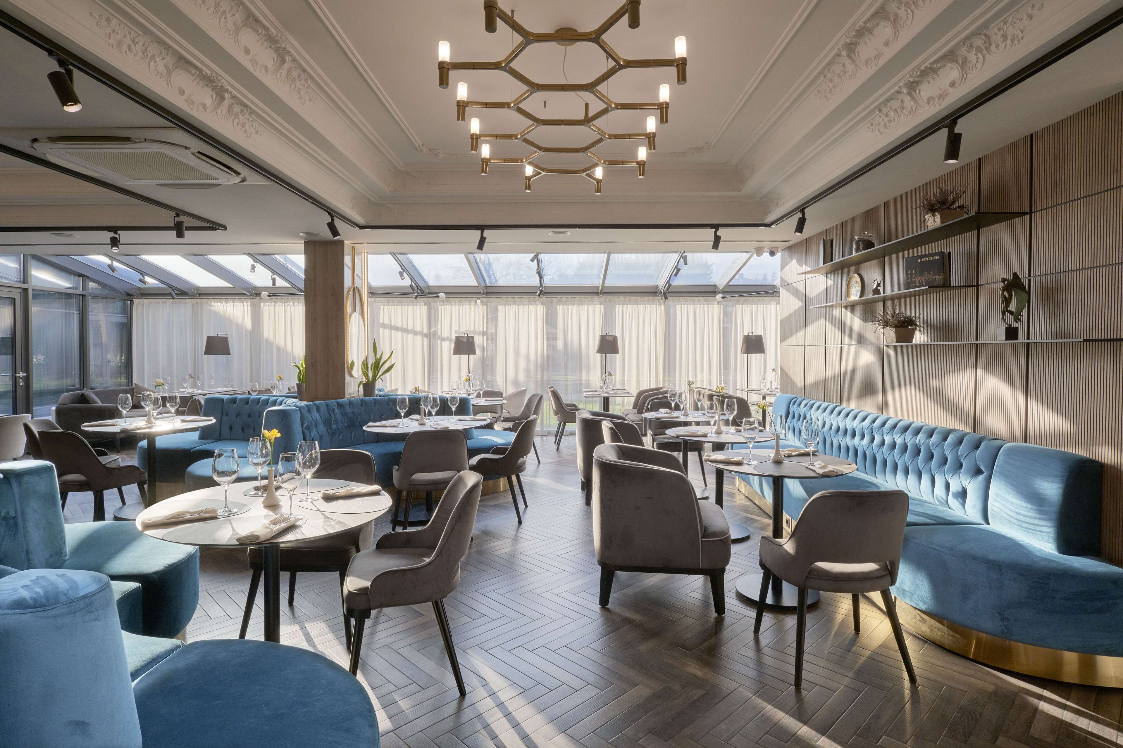 Un restaurant moderne avec des tables rondes, des sièges rembourrés en tissu bleu et un luminaire décoratif au plafond.