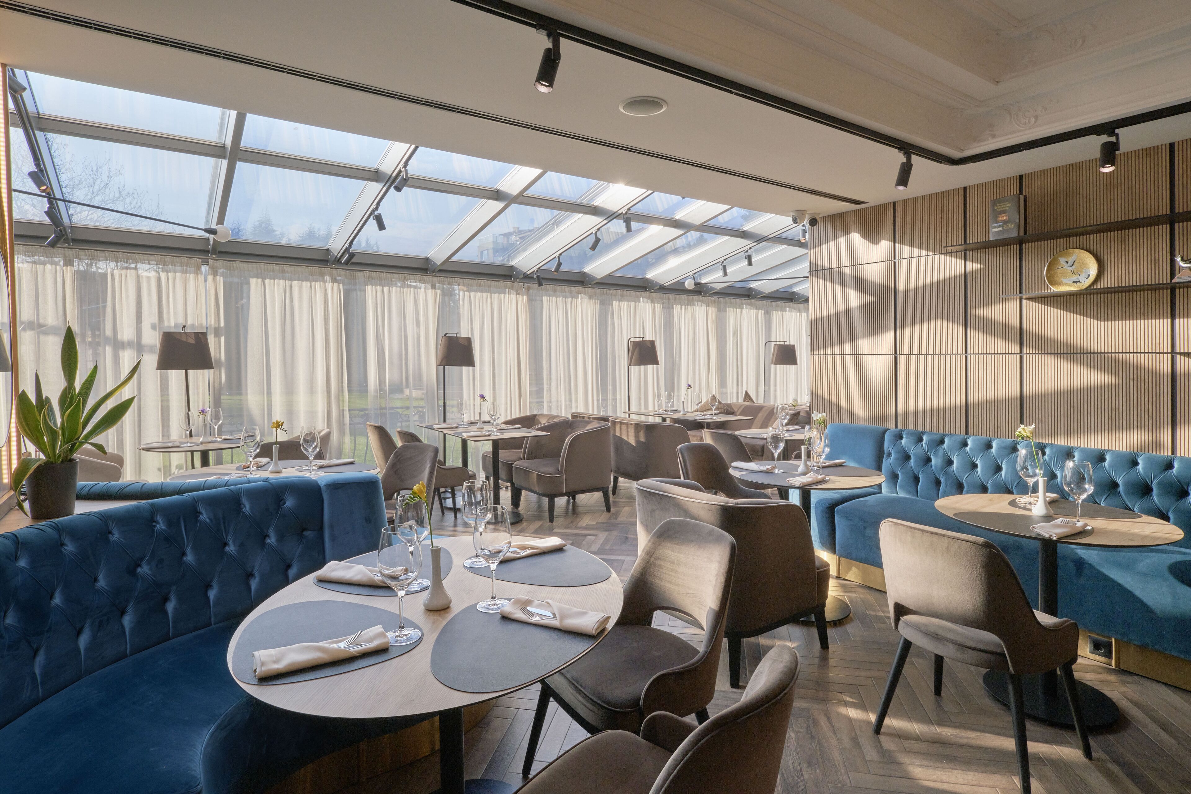 A restaurant with blue upholstered seating, round tables, and a glass ceiling allowing natural light.