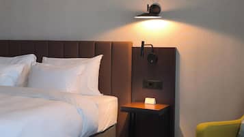 A hotel room with a bed, bedside table, lamp, and a yellow armchair.
