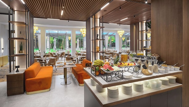 Un espace repas moderne doté d’un buffet, de sièges orange et de grandes fenêtres offrant une vue sur la verdure.