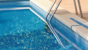 A swimming pool with a metal ladder, surrounded by a low hedge and a beige wall. - Hotel JS Horitzo (Santa Margalida)
