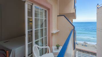 A balcony with a view of the ocean, a small table with a plant, and a white chair.