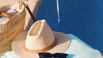 Una toalla de playa, un sombrero de paja, gafas de sol y un bolso tejido junto a una piscina.